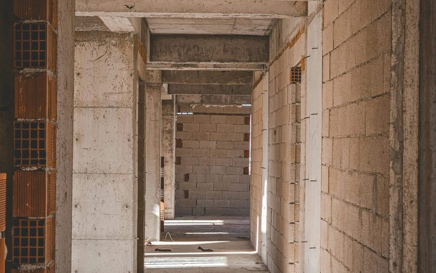 A natural light corridor in an unfinished concrete building with exposed brick walls.